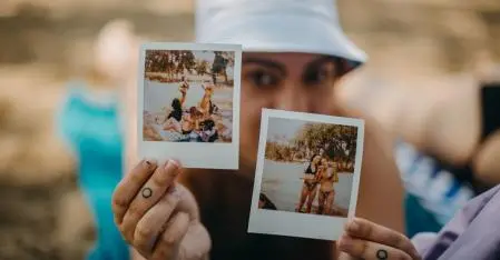 woman holding two polaroid pictures, her face is blurred in the background