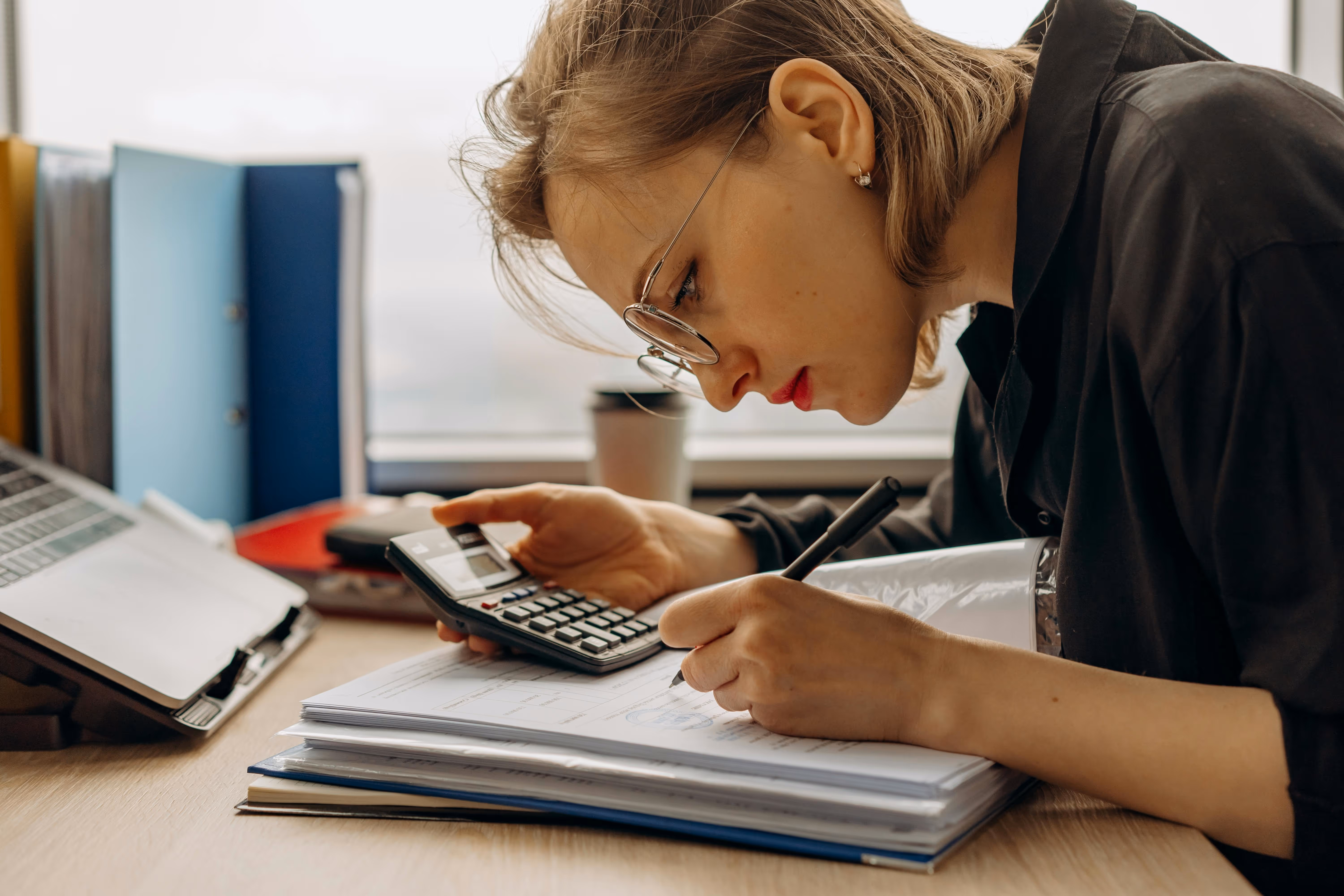 A Woman Writing on a Book while Holding a Calculator