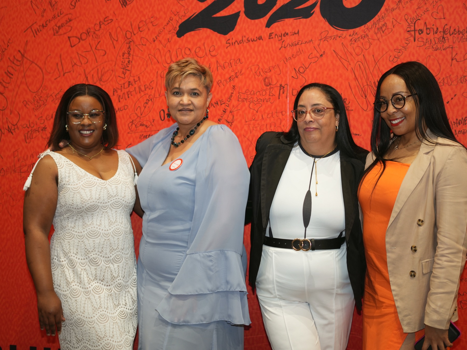 Four attendees together at the orange Miko & Anna conference backdrop