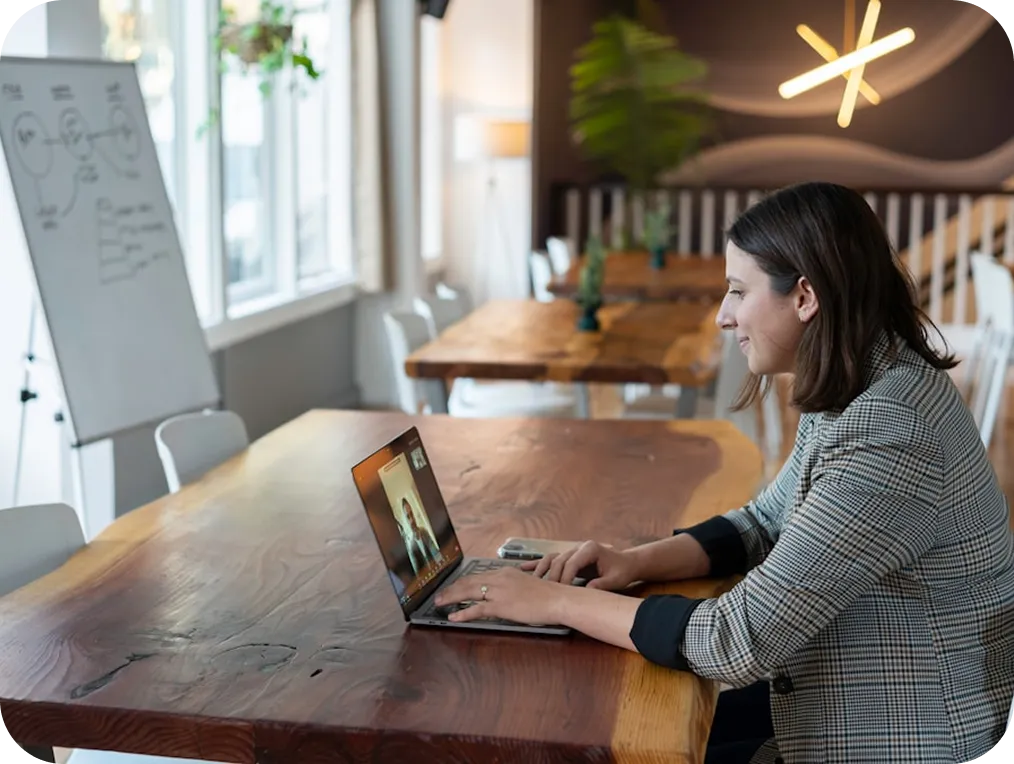 A woman in a plaid blazer participates in a video call on her laptop in a modern office setting