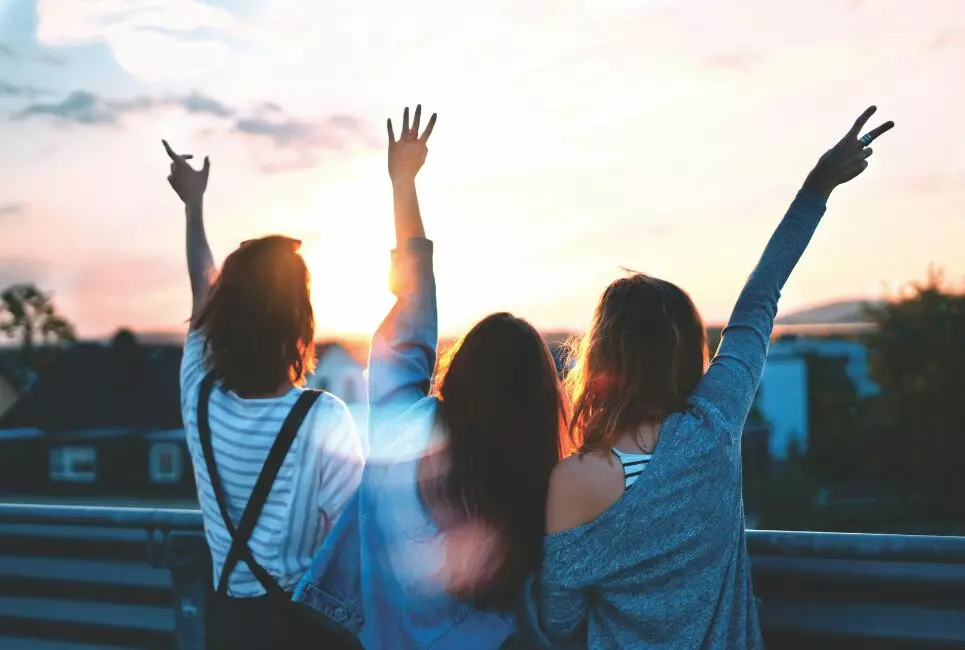 Back of three friends raising hands up in air