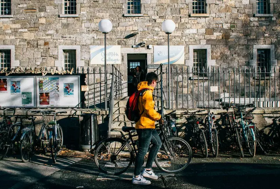 Student with yellow jacking parking bike outside Dublin college
