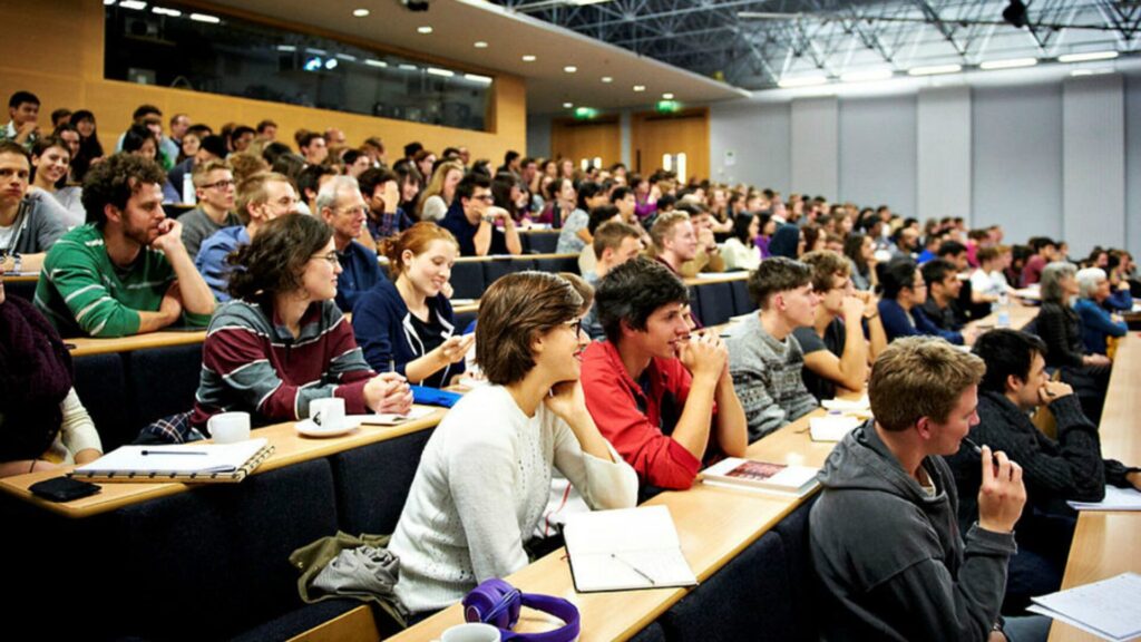A group of students sitting in a classroom, staring at the front, and smiling