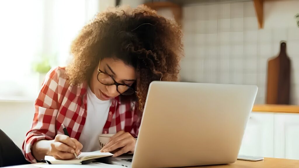 A student taking an online class on their laptop and taking notes