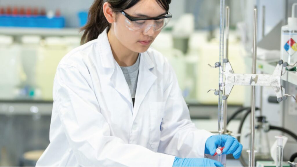 A student wearing a white labcoat and blue gloves and working in a lab