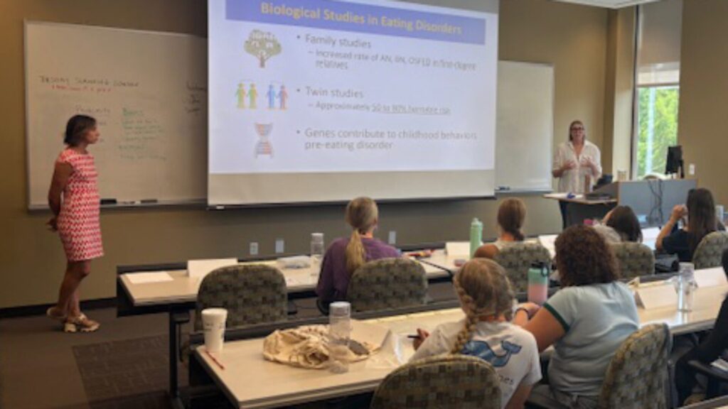 A group of students sitting in a classroom and watching an instructor present a psychology class