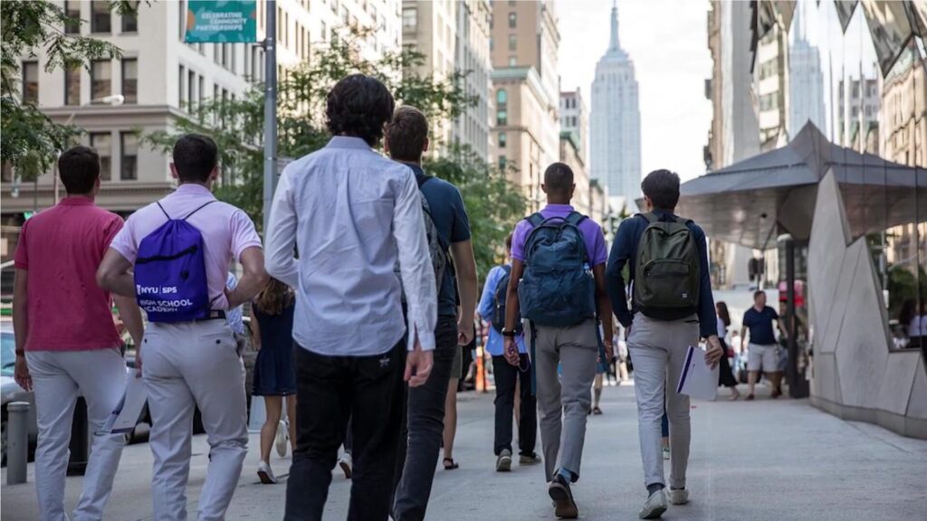 A group of six students walking on an NYC street with their backs to the camera