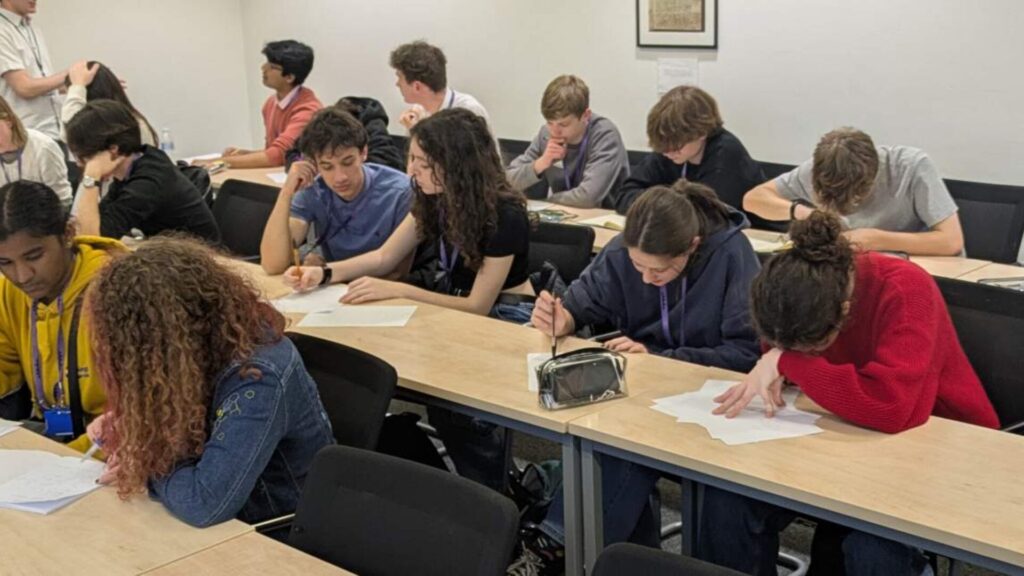 A group of students in a classroom, noting something down on papers