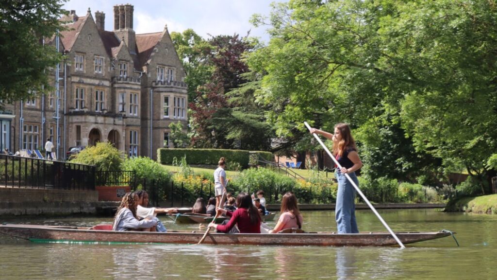 A group of students participating in boating in a lake next to a Oxford college campus