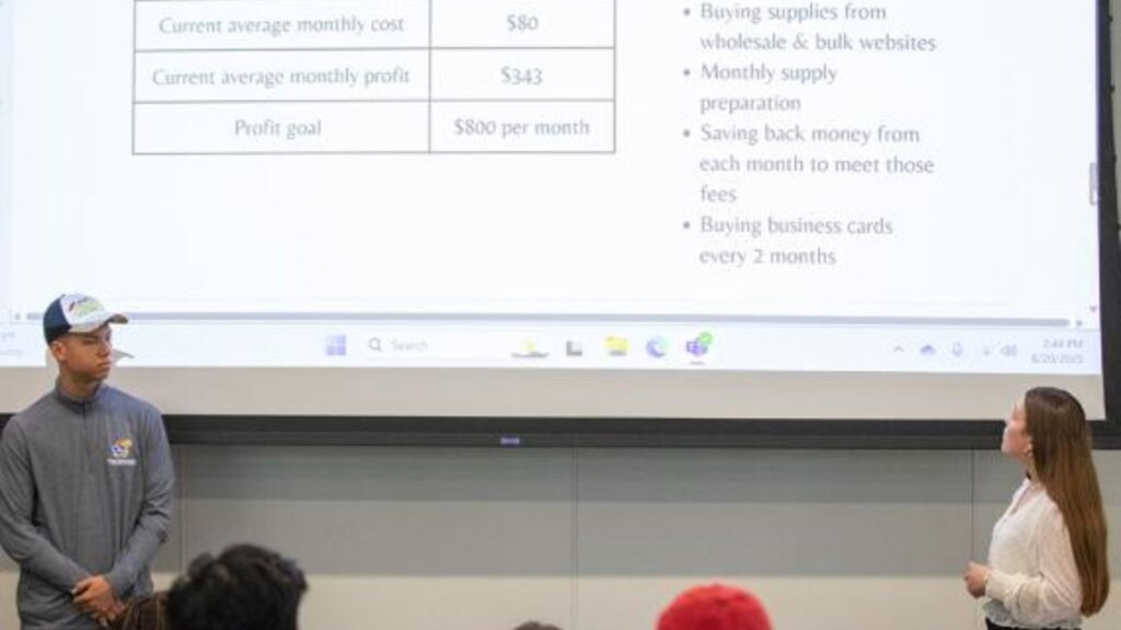 A duo of students explaining their business idea to a group of students in the crowd