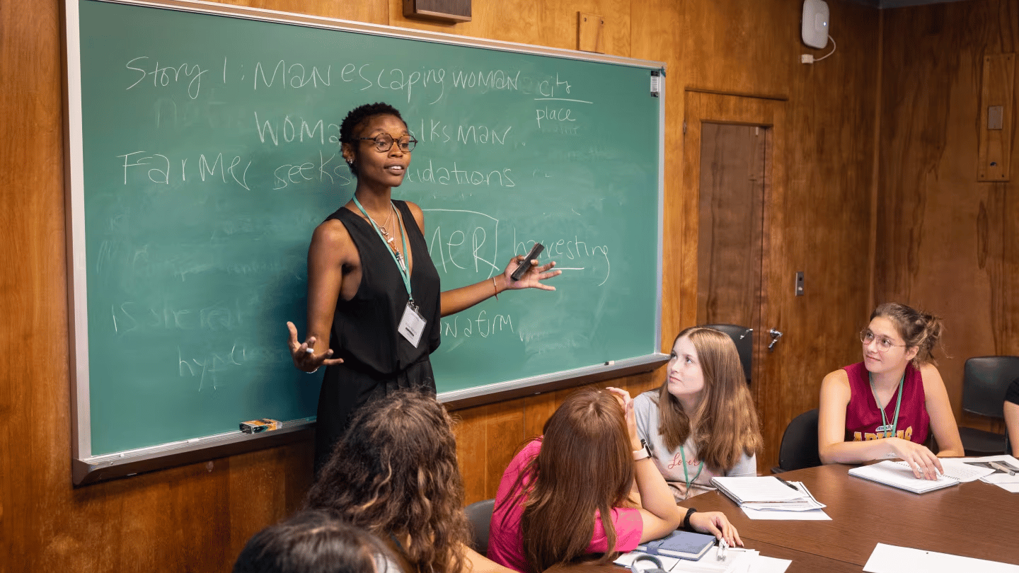 A group of students sitting in a class and listening to an instructor teach using a chalkboard