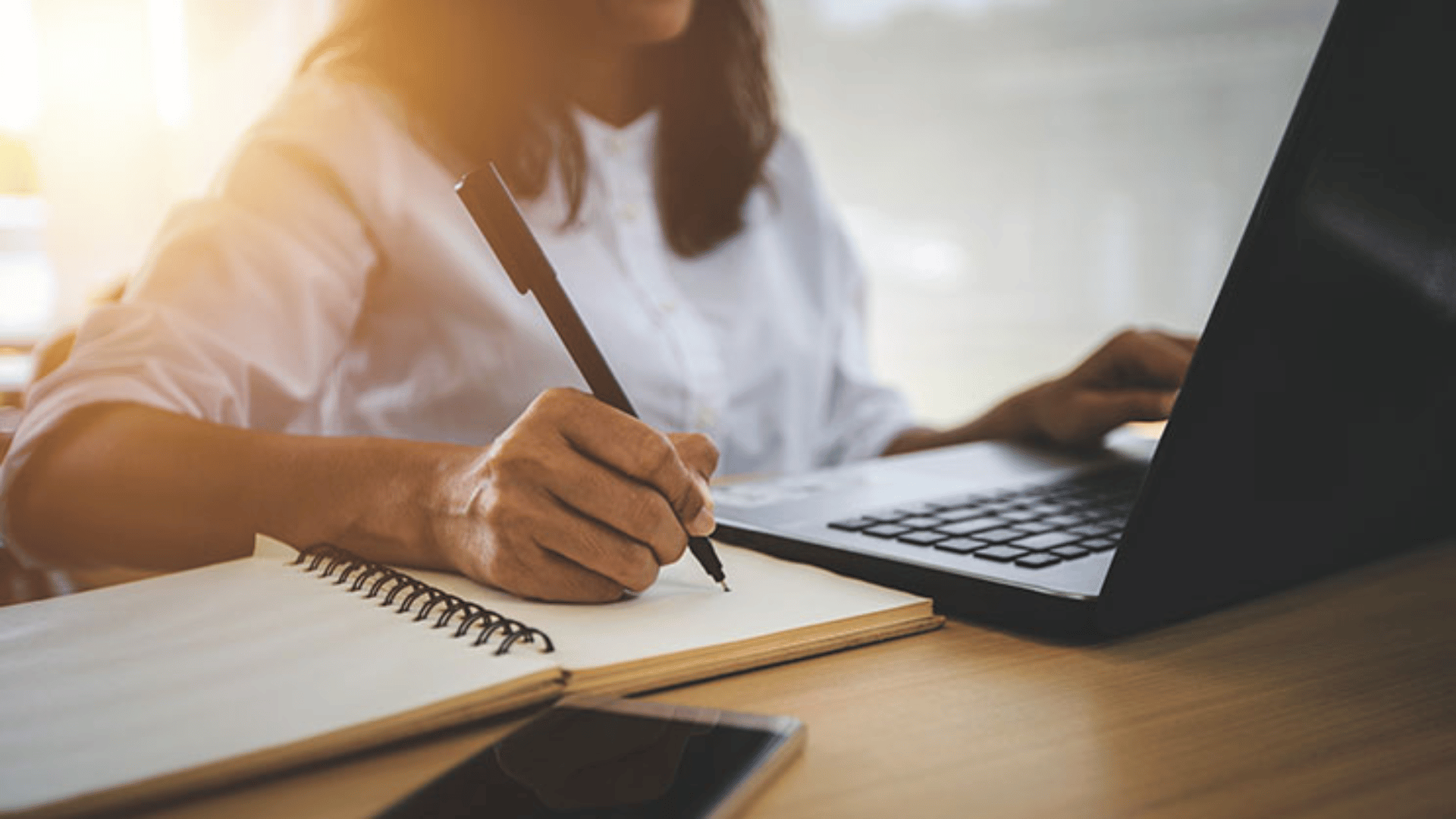 A student sitting in front of her laptop and taking notes in her notebook