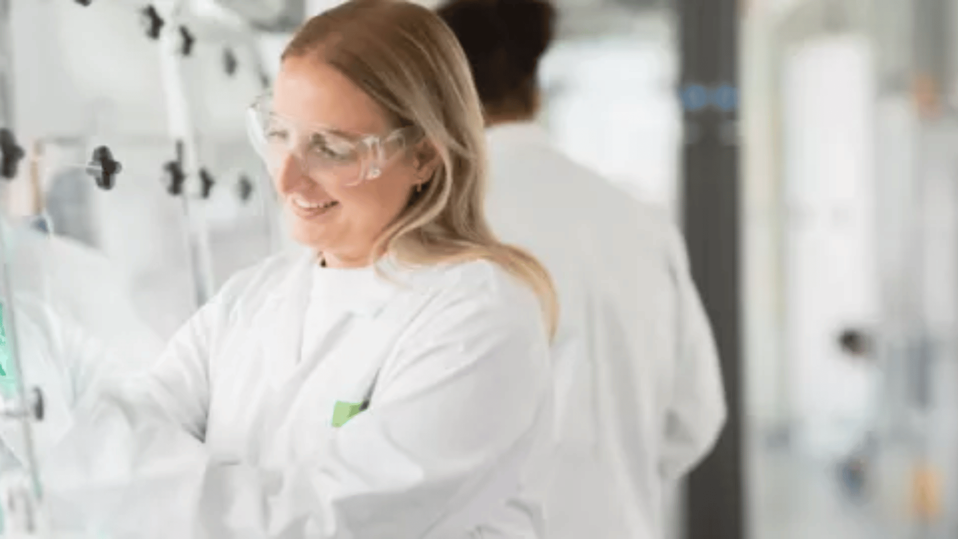A student wearing a lab coat and green gloves and performing an experiment