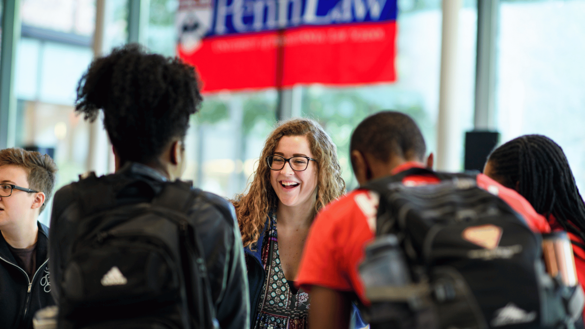 A group of students laughing together with a PennLaw banner in the background