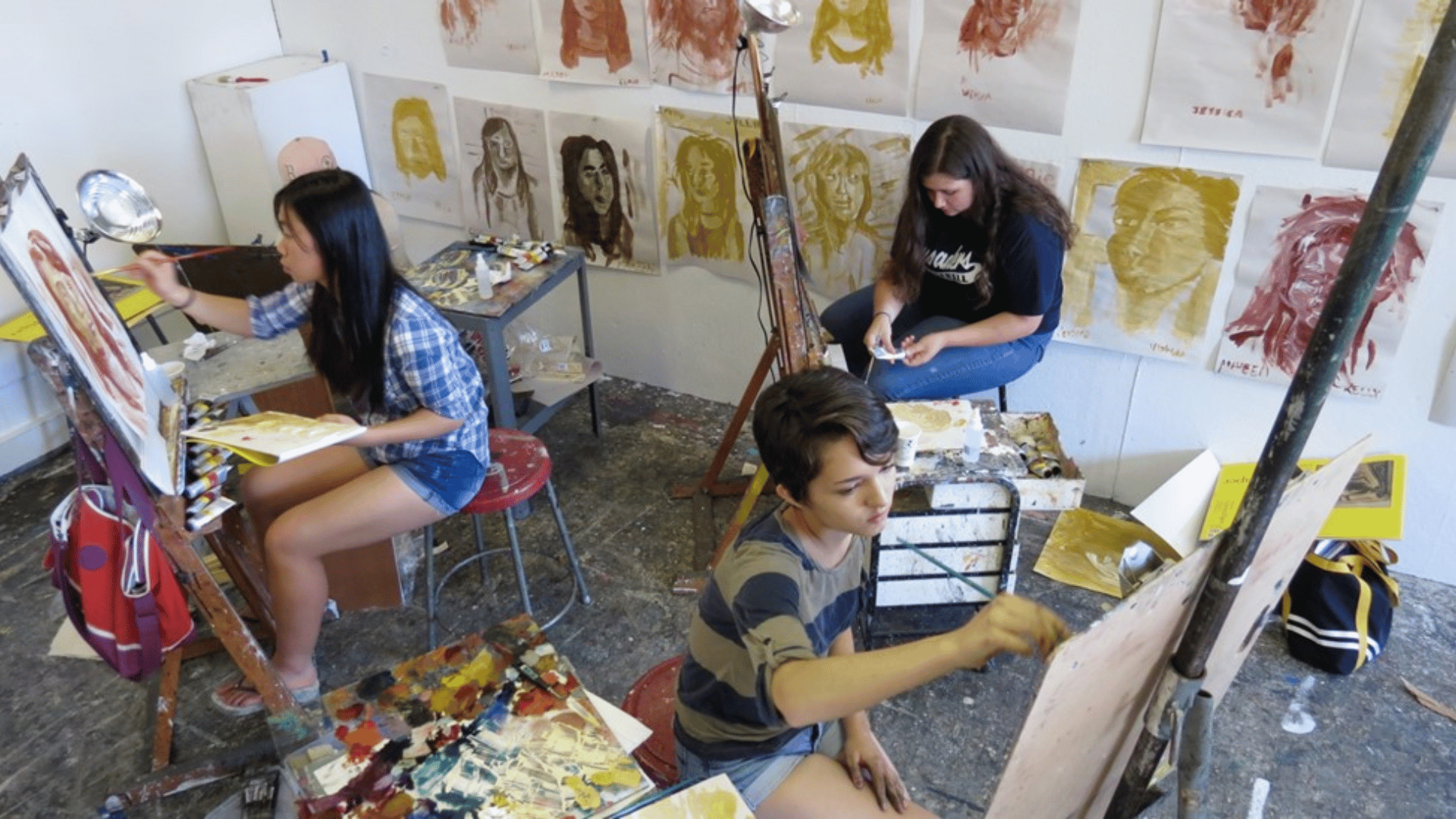 Three students sitting in a studio and making paintings