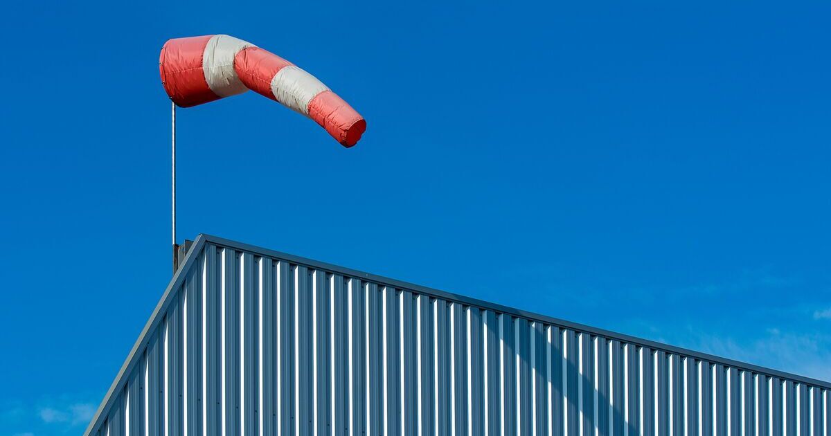 Red and white windsock extended horizontally in strong wind above a metal building against a clear blue sky