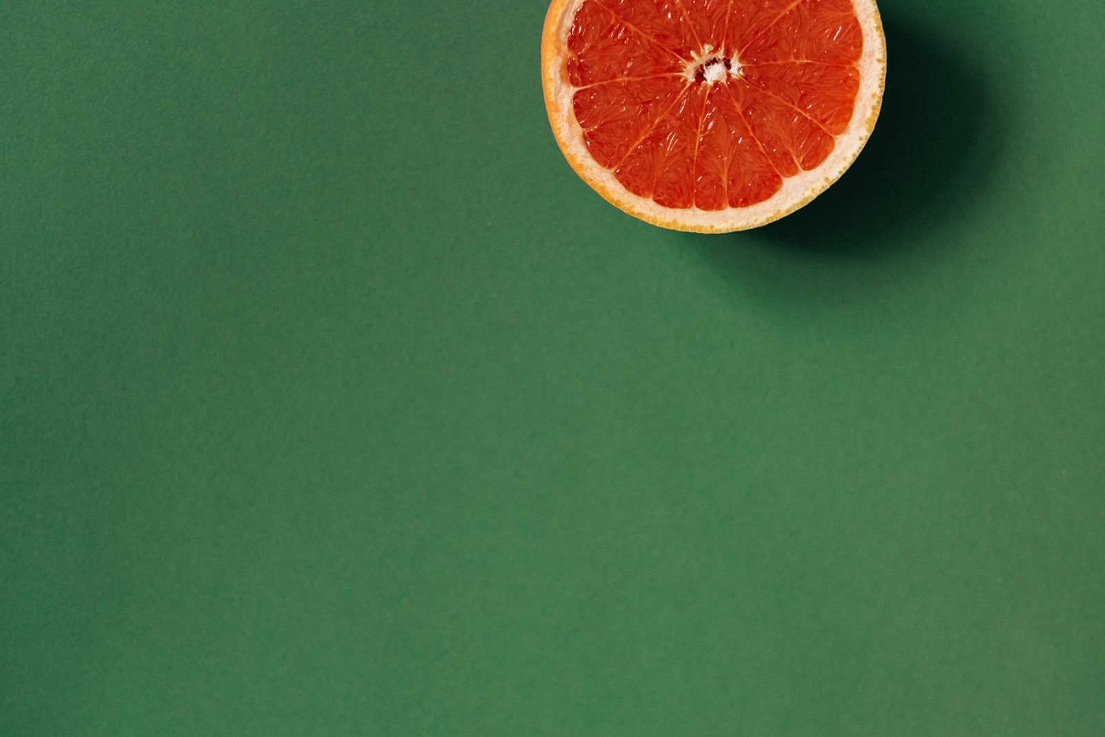 Auf dunkelgrünem Grund befindet sich eine Hälfte von der Frucht Grapefruit.