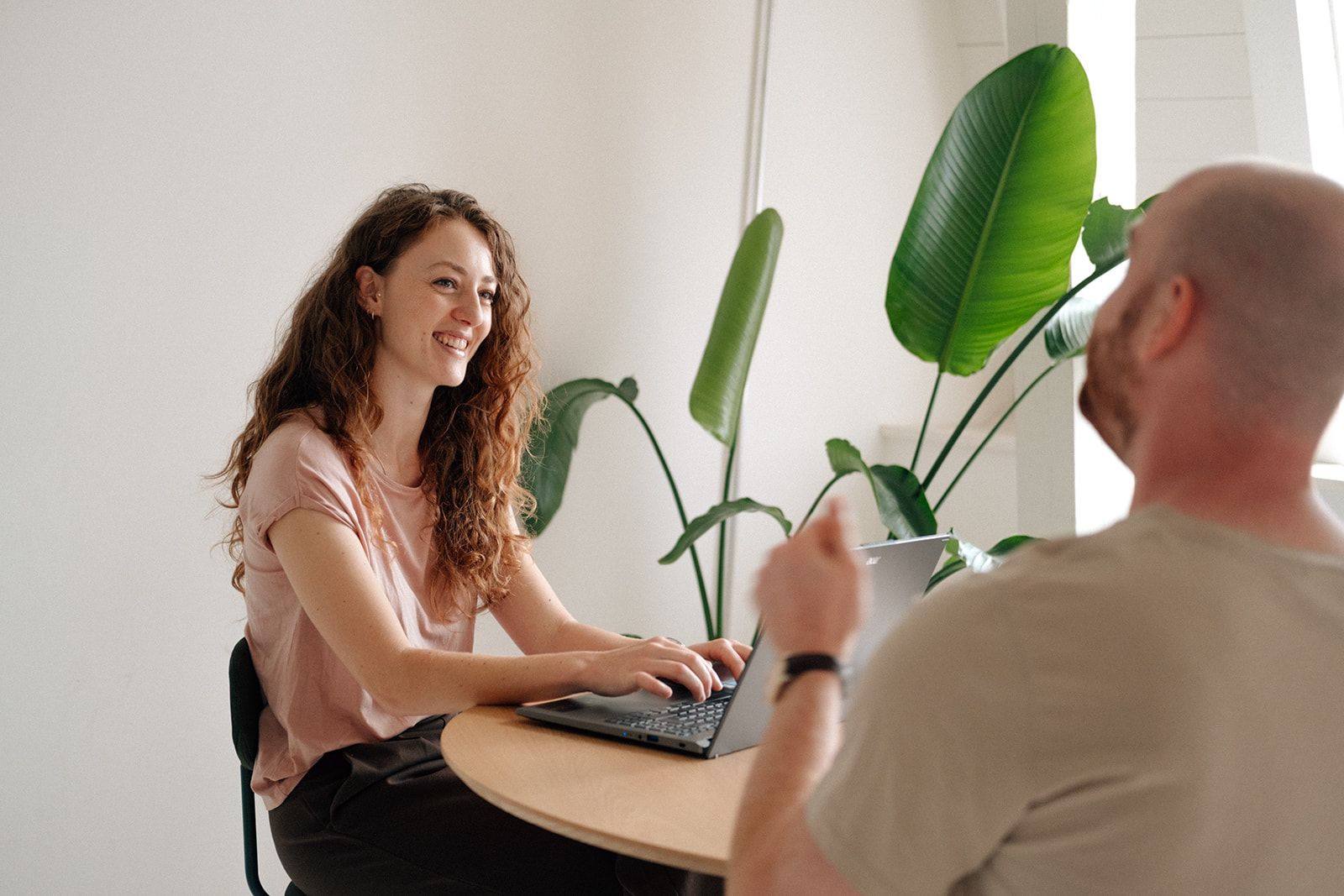 Eine Ernährungsberaterin berät einen Patienten. Der Patient und die Ernährungsberaterin sitzen beide an einem Tisch. Der Patient spricht und die Ernährungsberaterin hört lächelnd zu. Sie bedient dabei ihrem Laptop vor ihr.
