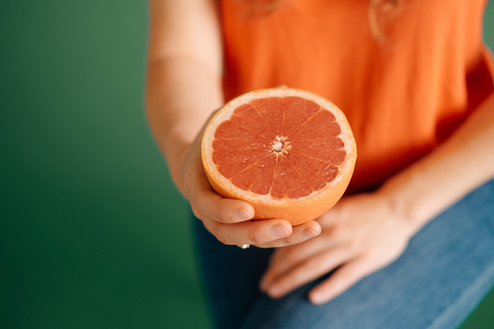 Eine Frau hält mir einer Hand eine Hälfte einer Grapefruit.