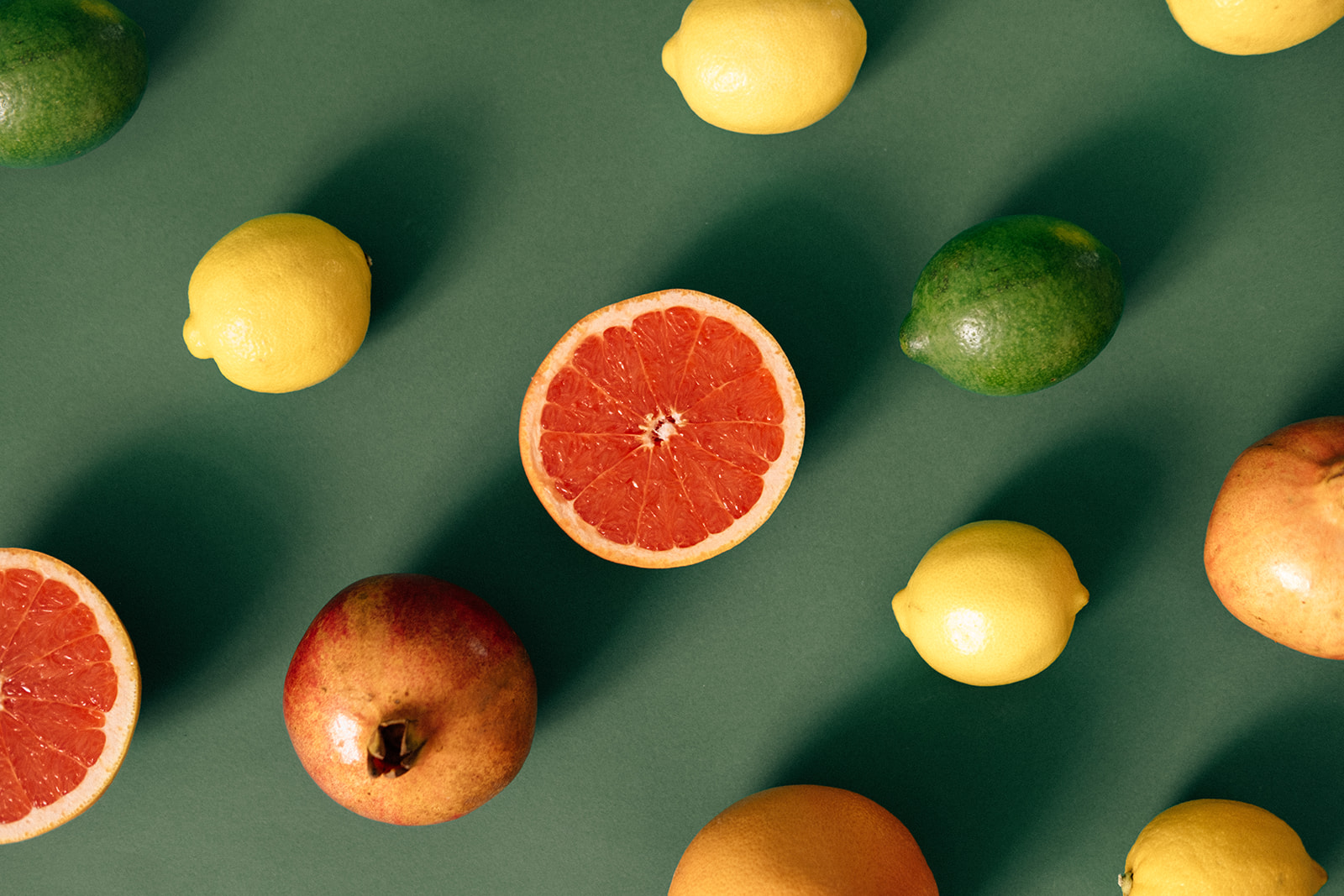 Auf grünem Untergrund befinden sich verschiedene Früchte. Aufgeschnittene Grapefruit-Hälften, Zitronen, Limetten und Grapefruits.