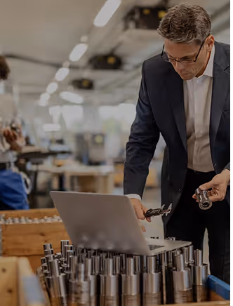 A man working on a laptop surrounded by metal parts.
