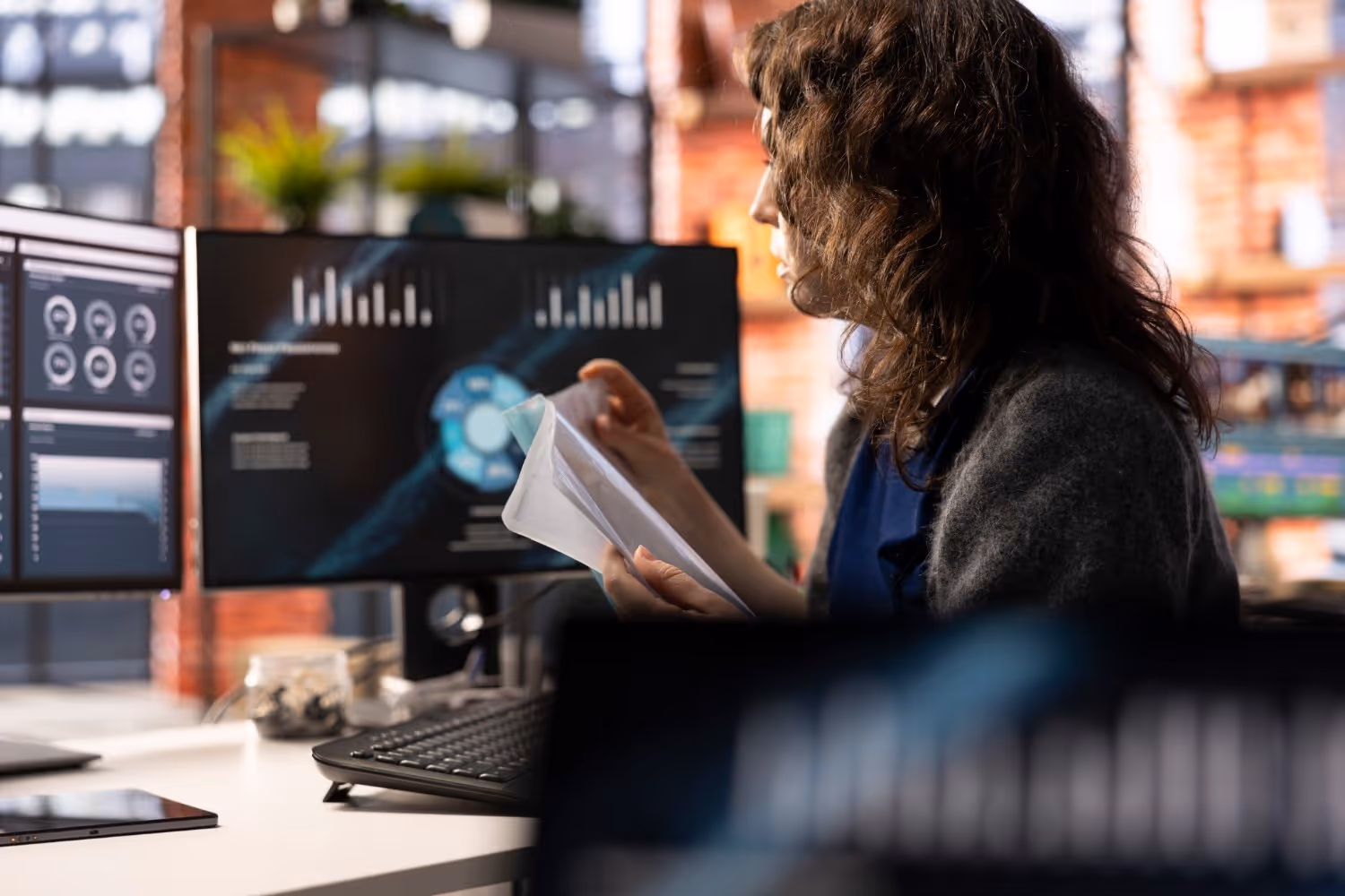 A woman comparing notes on paper with the data on a computer screen