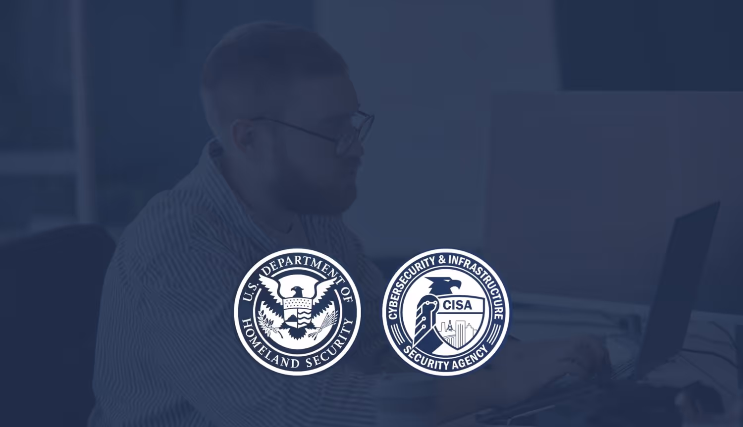 A slightly greyed out picture of a man working on a laptop. Stamped on top of the image are two logos: the U.S. Department of Homeland Security and the Cybersecurity & Infrastructure Security Agency.