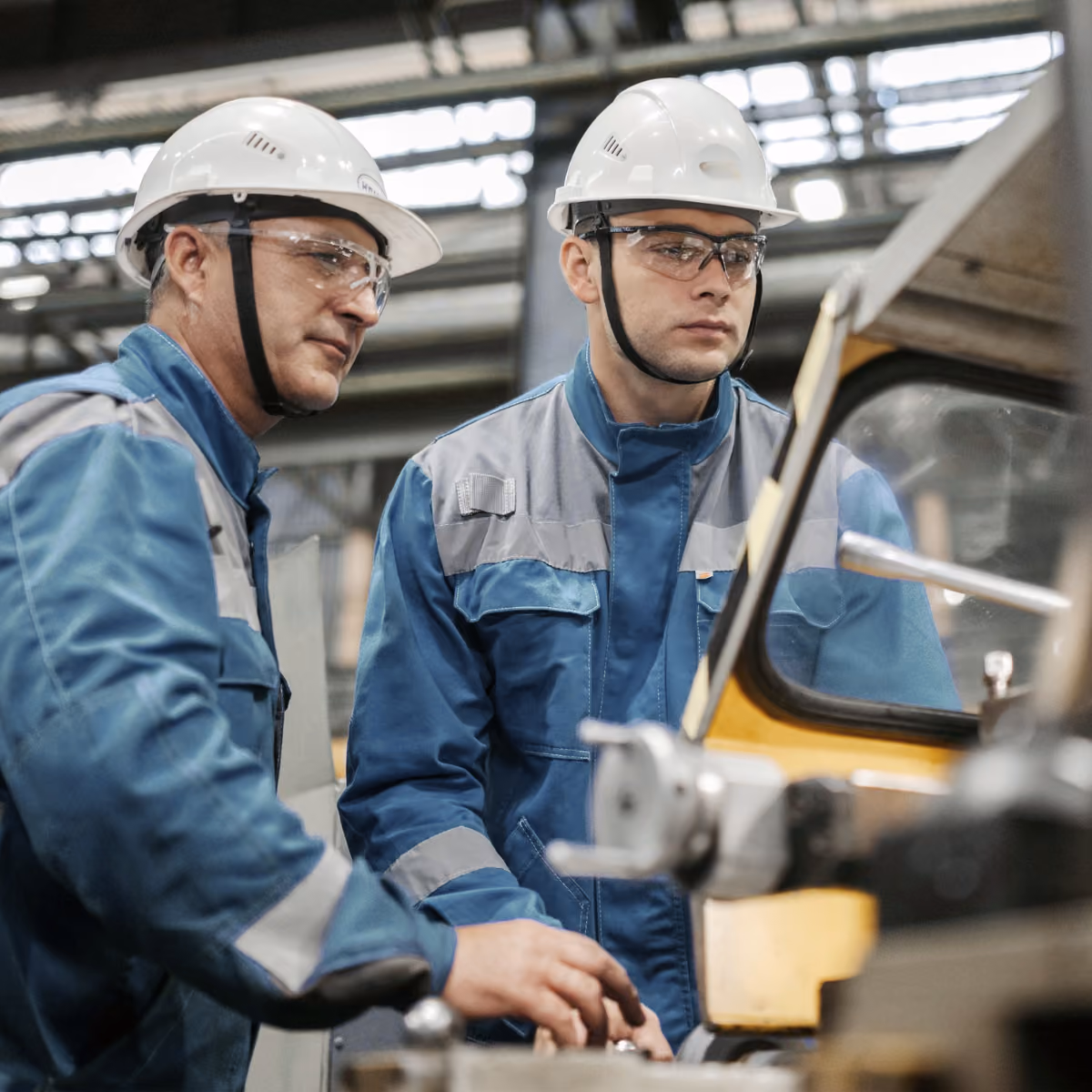 Two workers with helmets on the shop floor setting up a machine