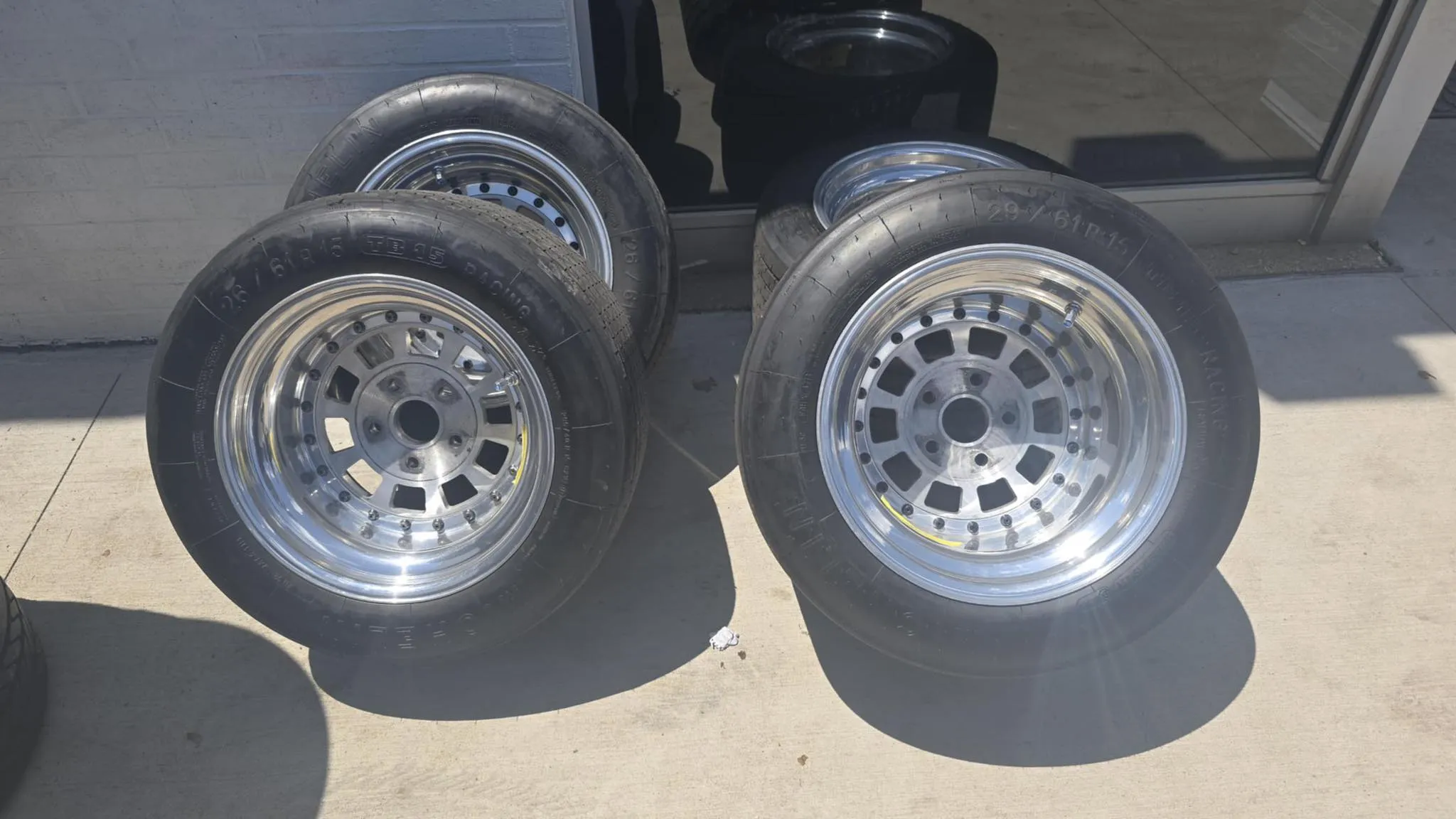 Two sets of racing wheels with tires displayed outdoors, featuring metallic rims and visible tread patterns.