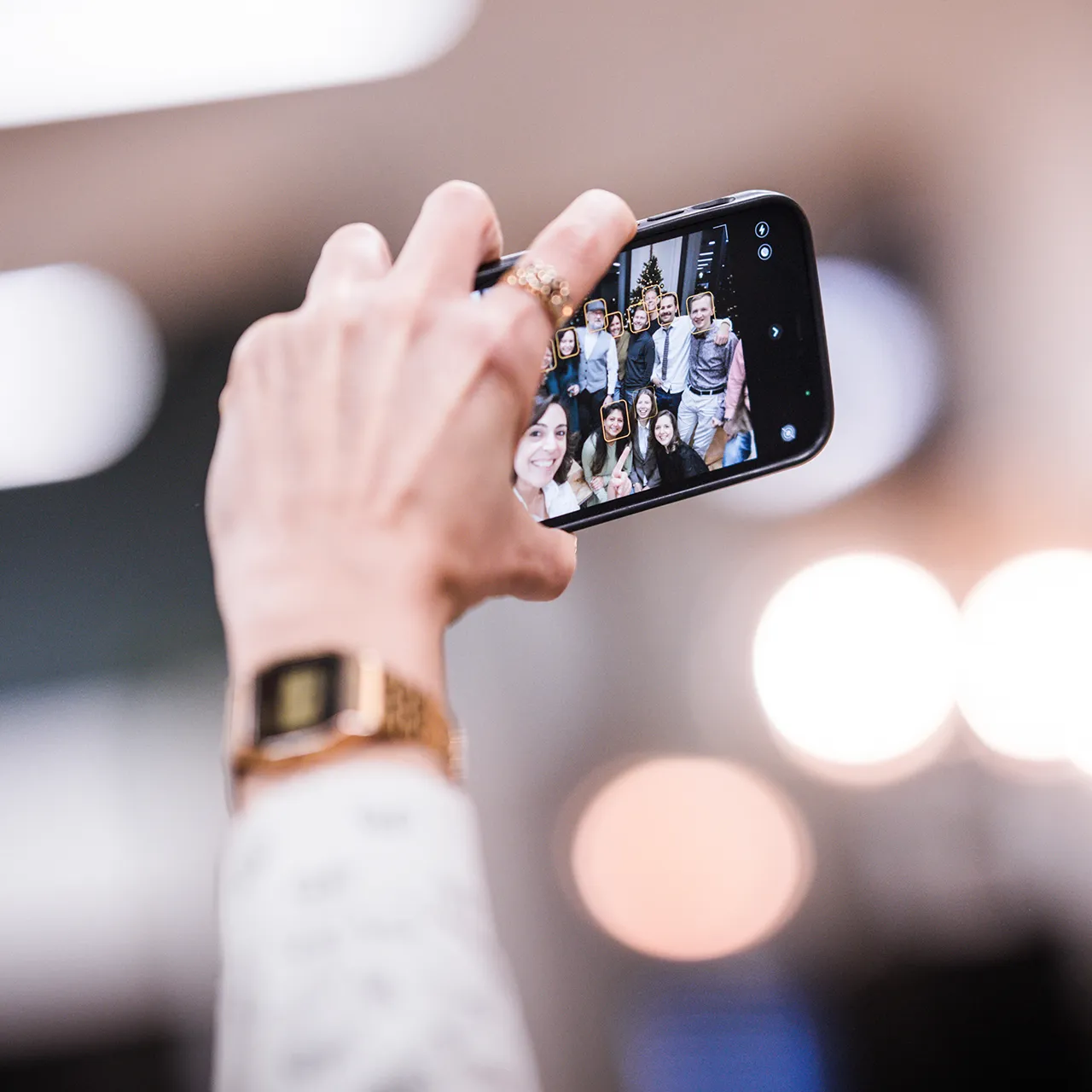 Close-up of a hand holding a phone taking a selfie of a smiling group of people.
