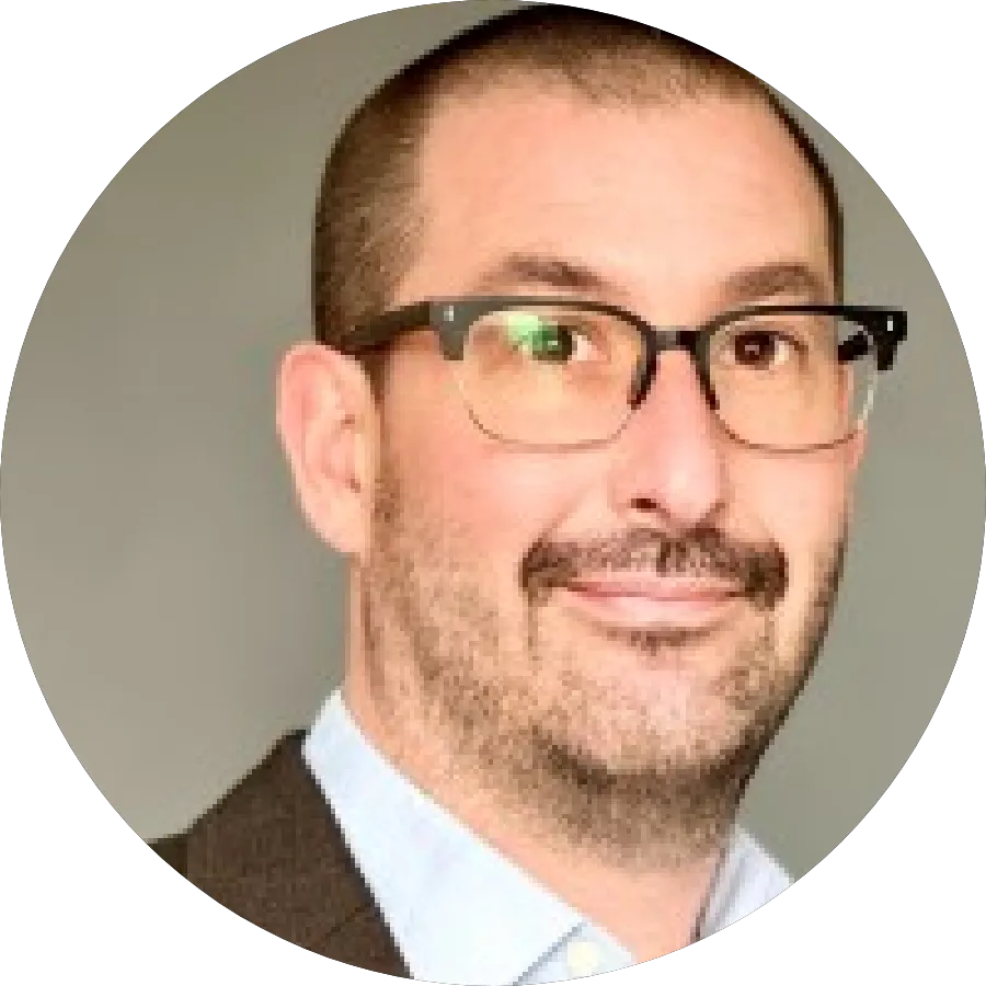 Smiling bald man wearing a blue hoodie with 'Agent Blazer' text and a logo patch on sleeve against a gray background.