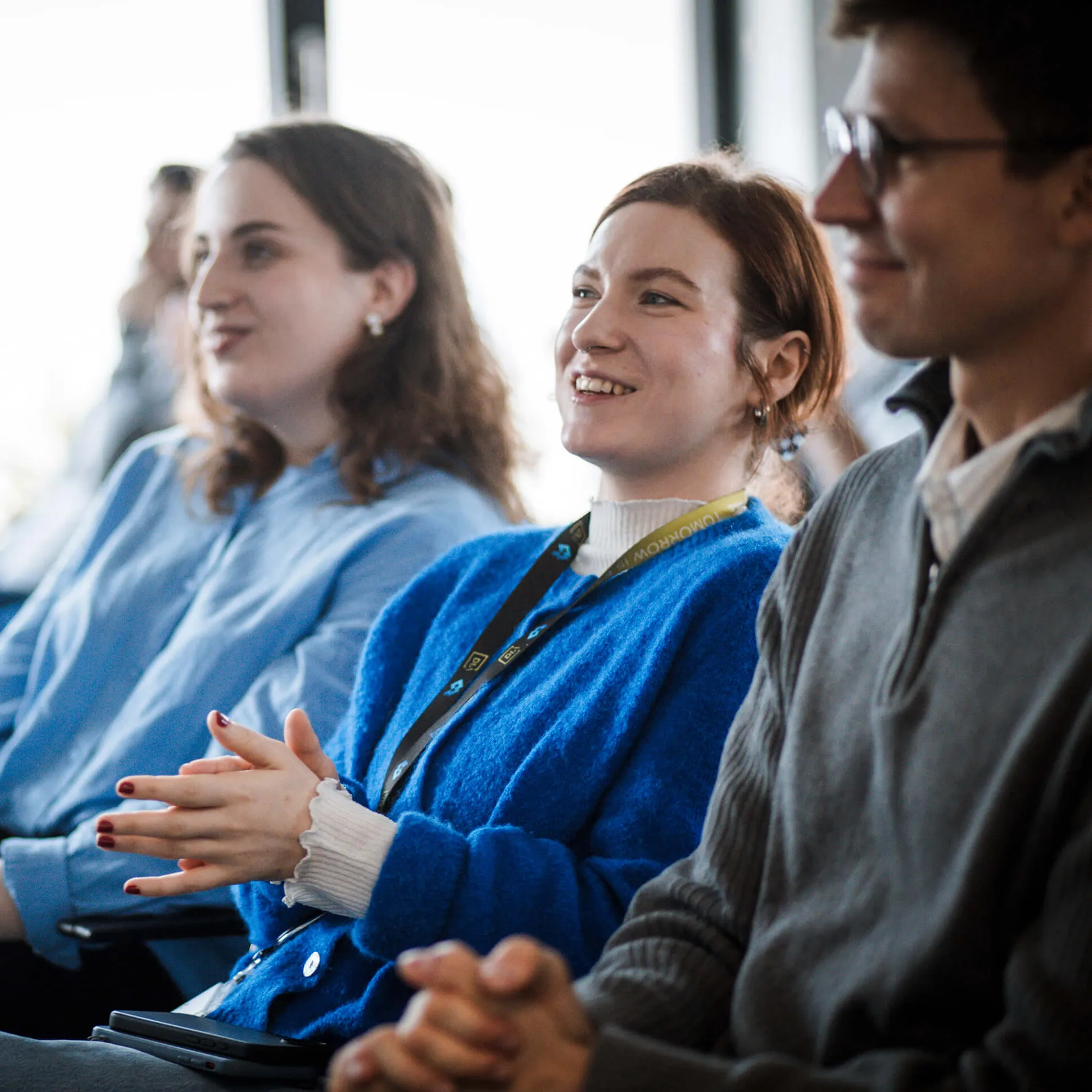 Three people engaged in a discussion around a table with a laptop, coffee cup, and plant in the center.