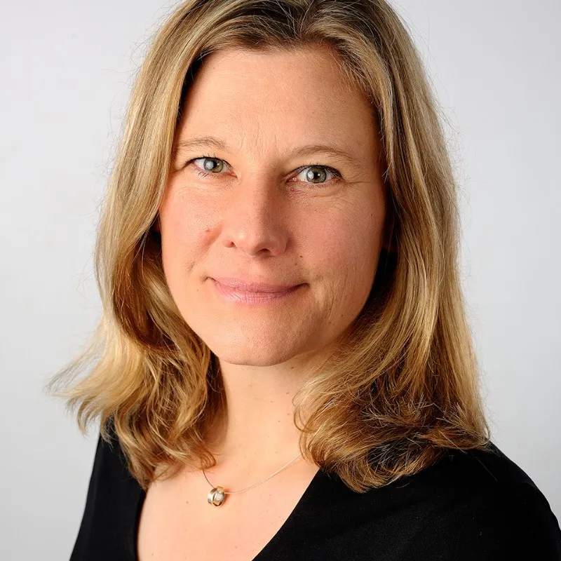 Smiling bald man wearing a blue hoodie with 'Agent Blazer' text and a logo patch on sleeve against a gray background.
