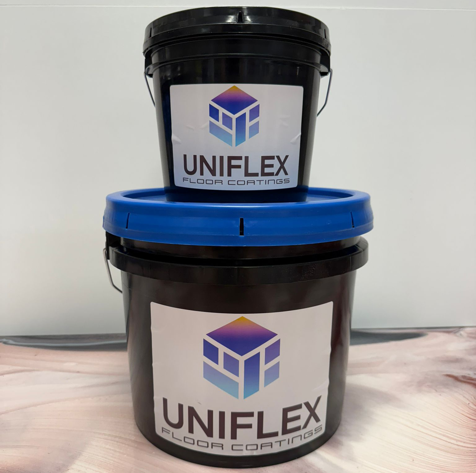 Two black buckets of Uniflex floor coatings stacked, the top bucket with a black lid and the bottom bucket with a blue lid.