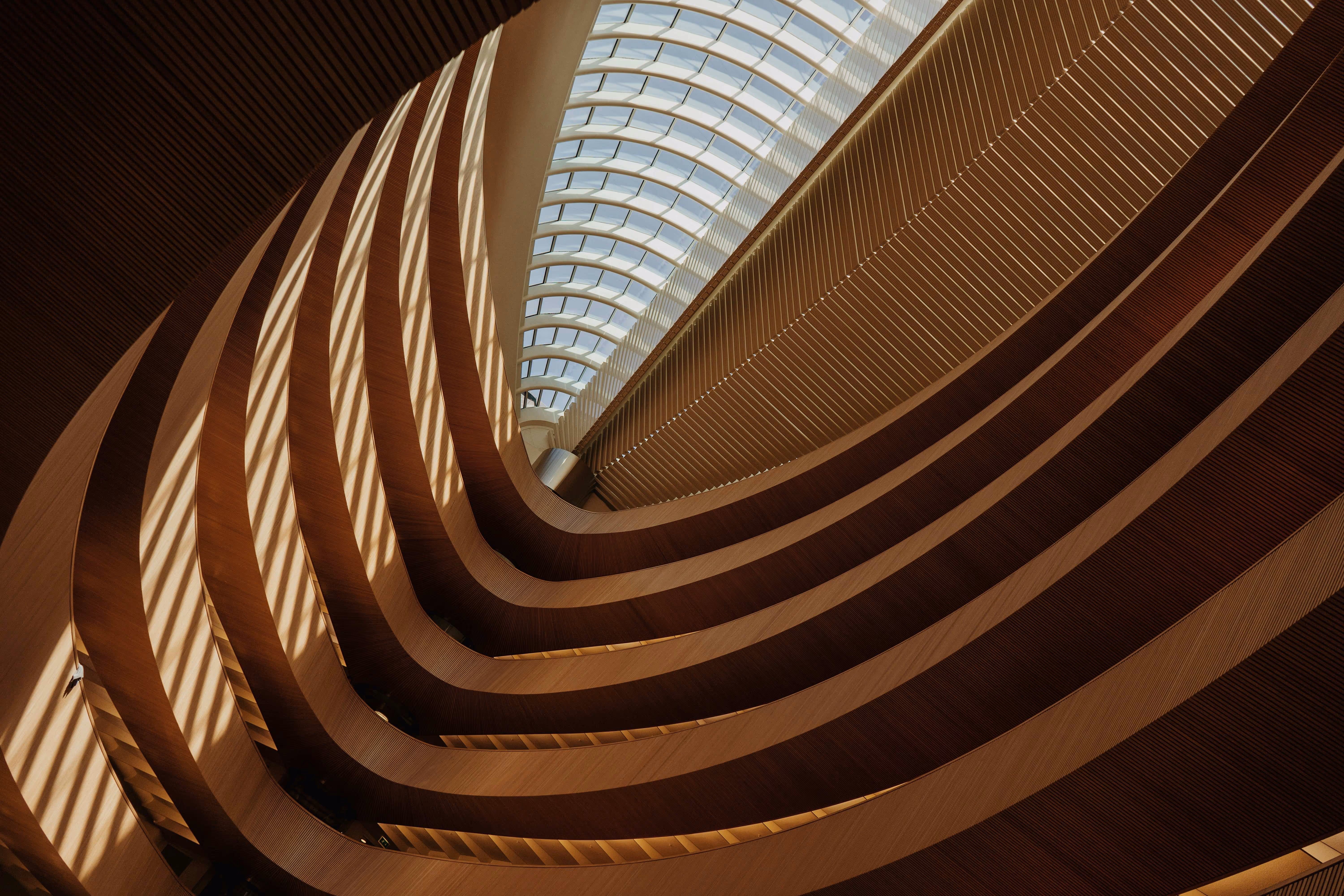 Spacious interior featuring curved wooden layers and natural light streaming through a large skylight above.