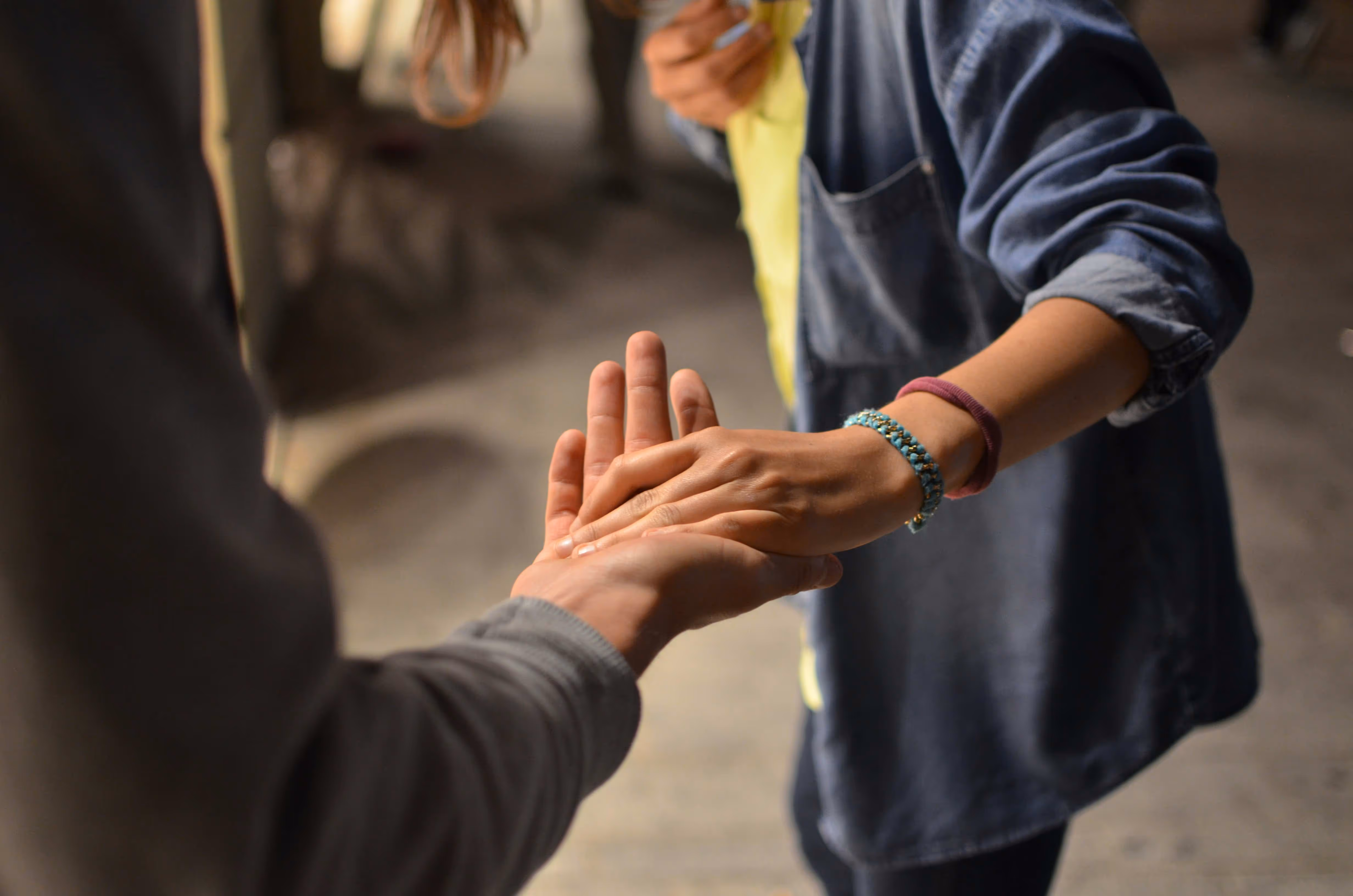 Two hands are reaching towards each other, one palm up and the other palm down, with bracelets visible on the wrist.