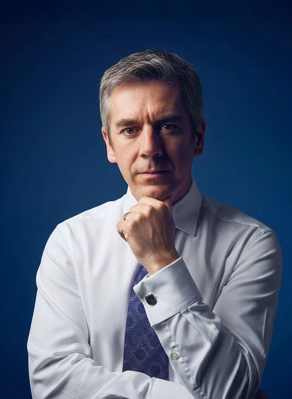 Maven Radd lawyer, Jonathan Garnett -  in a white shirt and purple tie, confidently posing with hand under chin against a blue background.