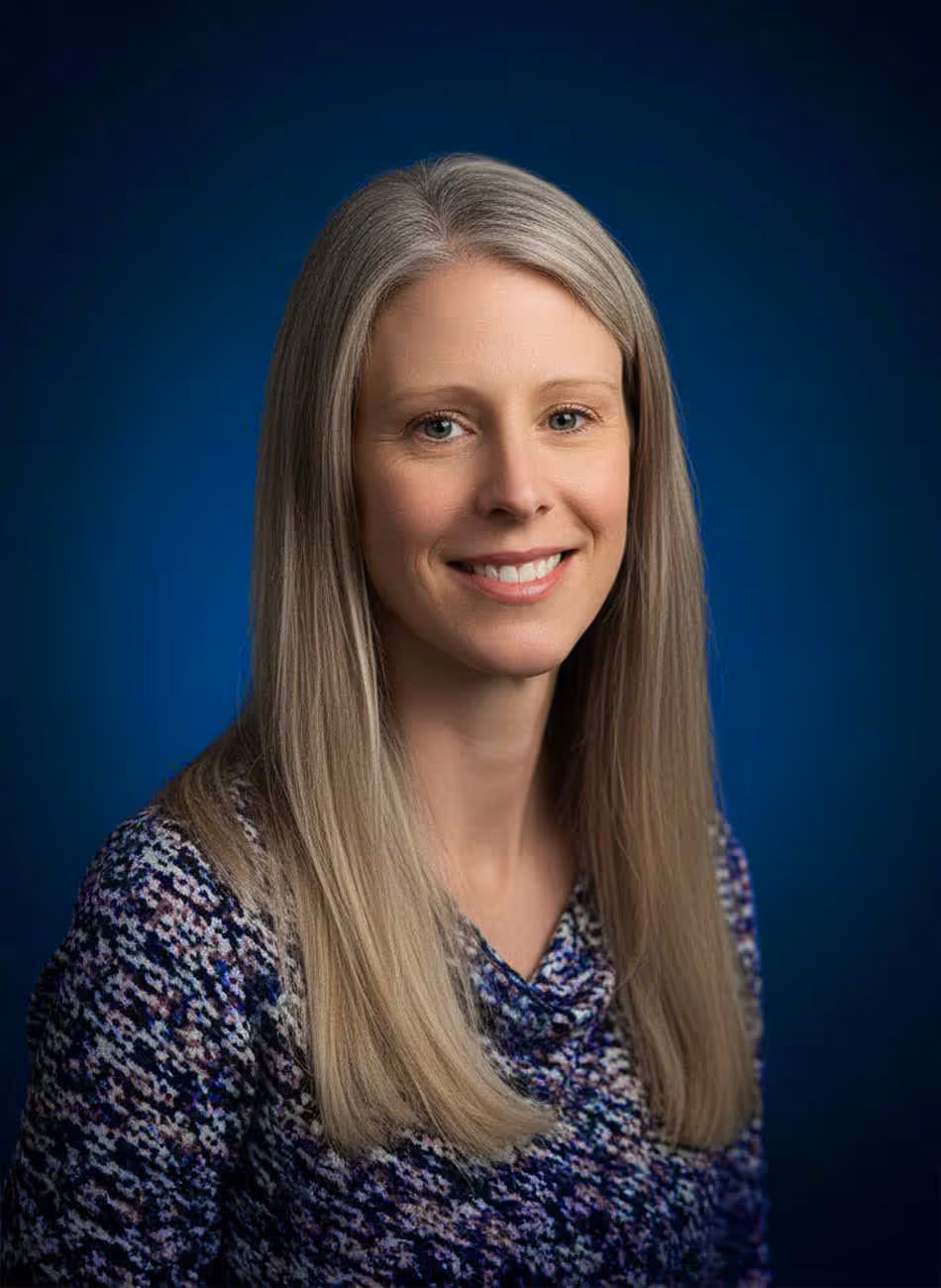 Gill Raw, Managing Director of Maven Radd, wearing a patterned sweater, smiling against a blue backdrop.