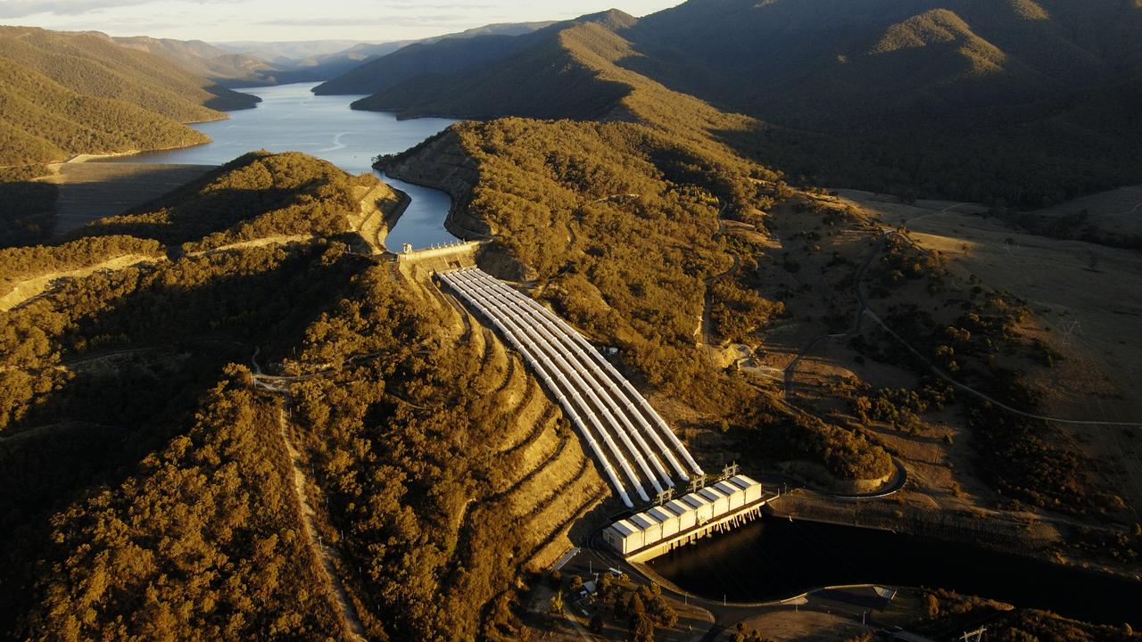 Aerial view of a dam nestled in hills, with a winding river and golden-brown foliage in the surrounding landscape.
