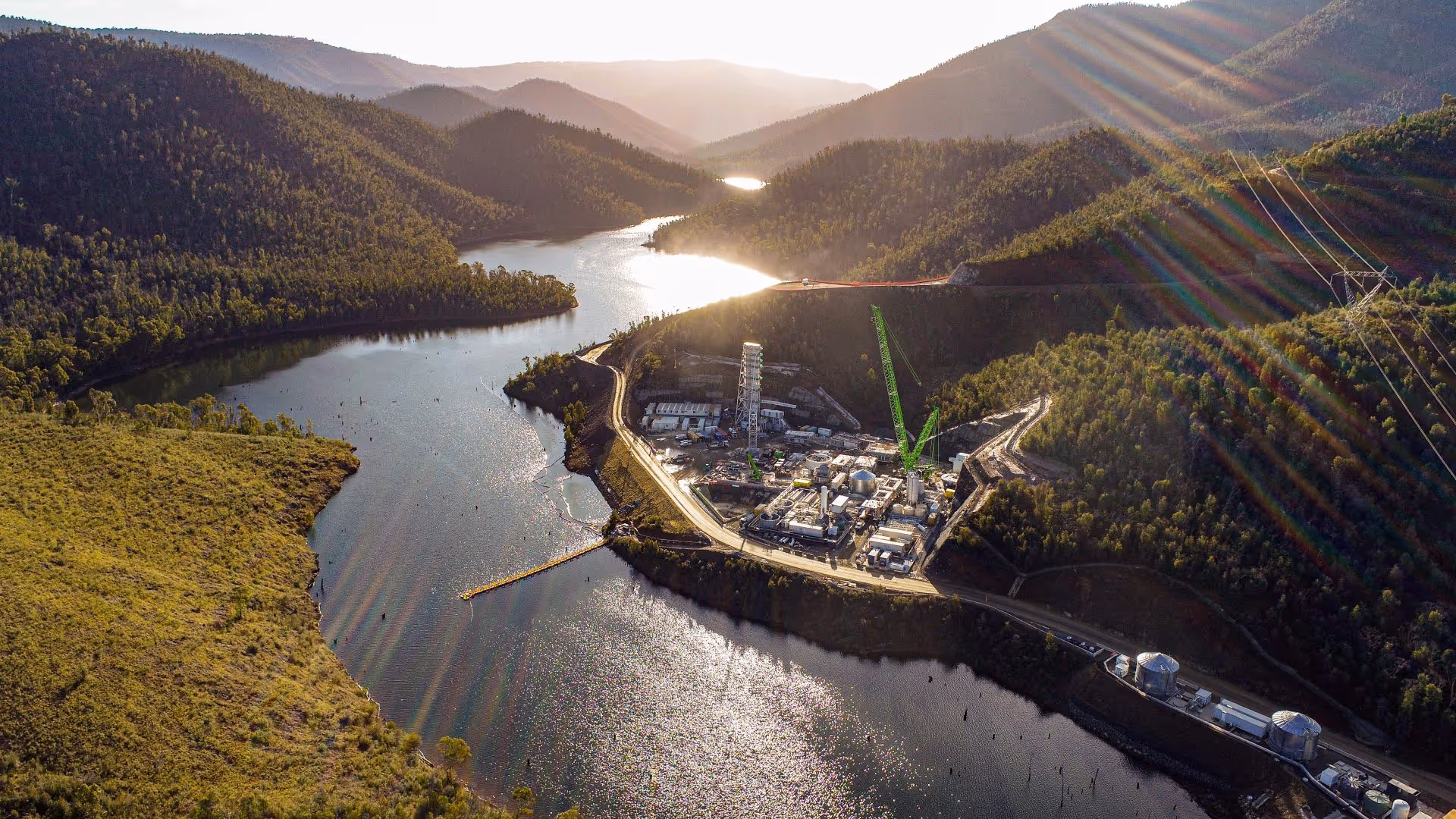 Carbon Capture project - Aerial view of a construction site near a river, surrounded by mountains and greenery, with cranes and industrial structures visible.