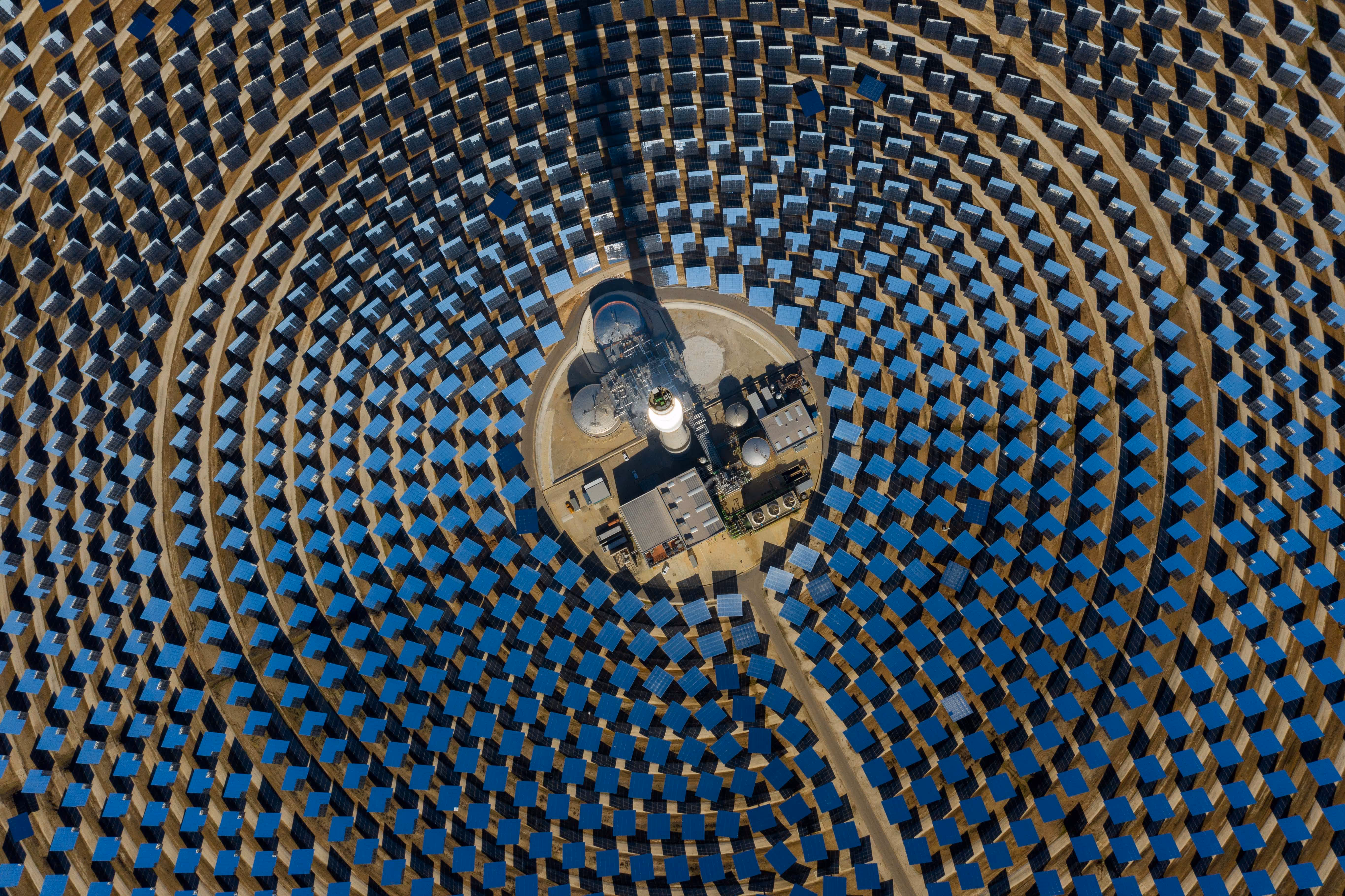 Aerial view of a solar power plant with concentric circular arrays of solar panels surrounding a central facility.