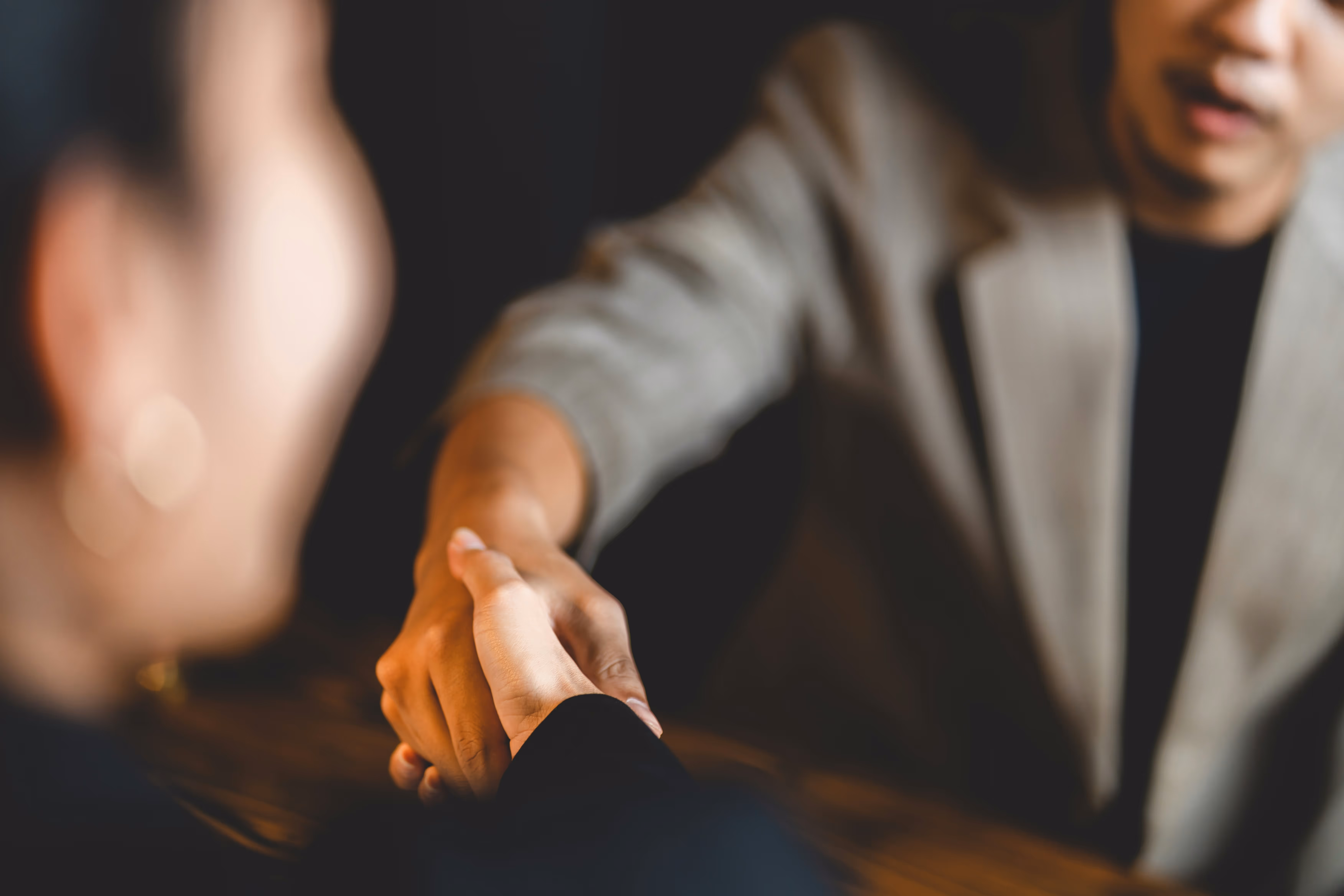 Two people are shaking hands in a close-up shot, conveying a sense of connection and agreement. The background is softly blurred.