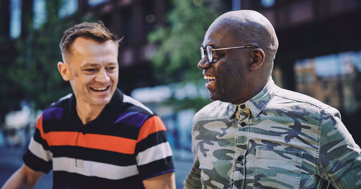 Change Grow Live, Maven Radd charity partner - Two smiling men are walking together outdoors, enjoying a cheerful moment. One wears a striped polo shirt, and the other a camo shirt.