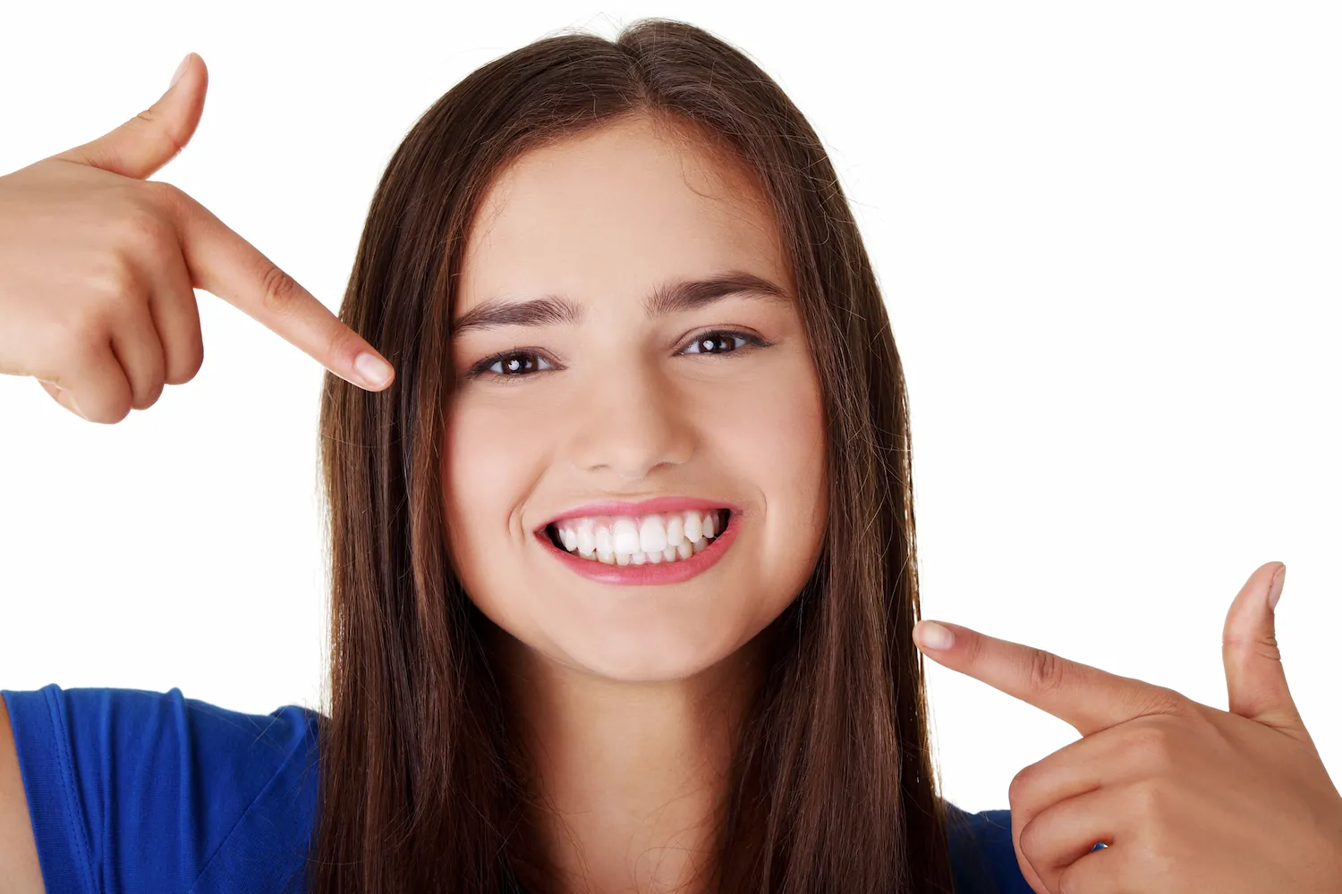 Smiling young woman with long brown hair pointing at her white teeth.