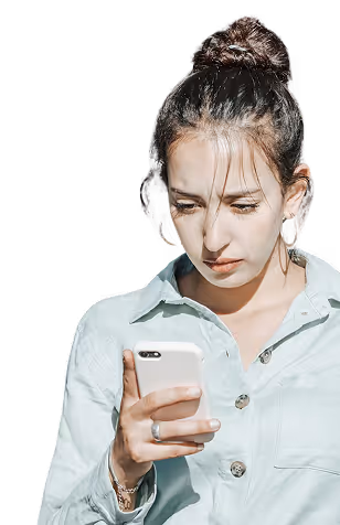 Une jeune femme coiffée d'un chignon, vêtue d'une chemise bleu clair, regarde attentivement son smartphone.