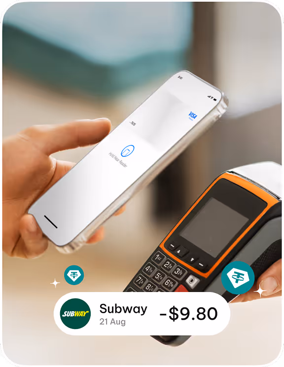 Person holding a smartphone near a card payment terminal to pay with crypto, showing a $9.80 Subway transaction.
