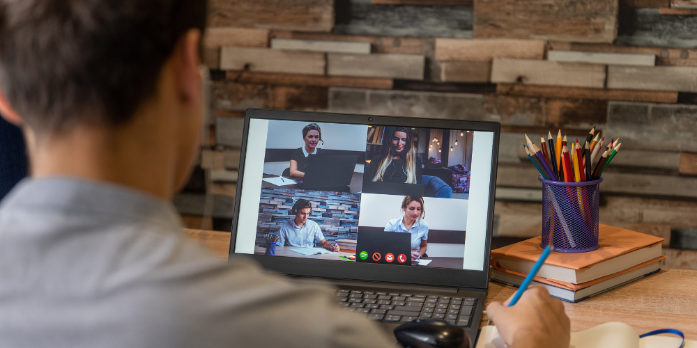 Over-the-shoulder view of a person attending a virtual meeting with diverse colleagues on a video call, illustrating the collaborative environment of a remote company.
