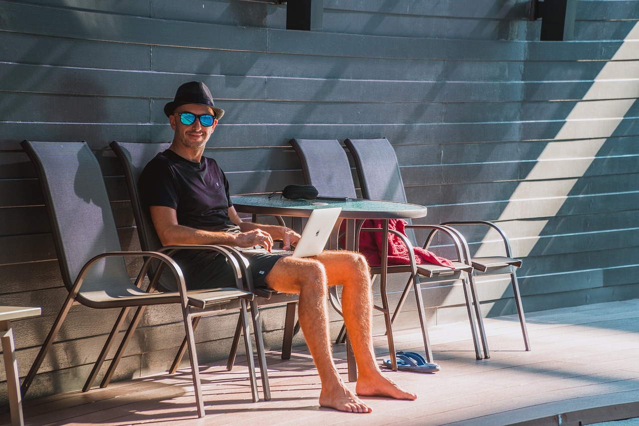 Man in a casual outfit working outdoors on a laptop, representing the flexibility and freedom of remote company culture, with a sunny backdrop suggesting a work-life balance.