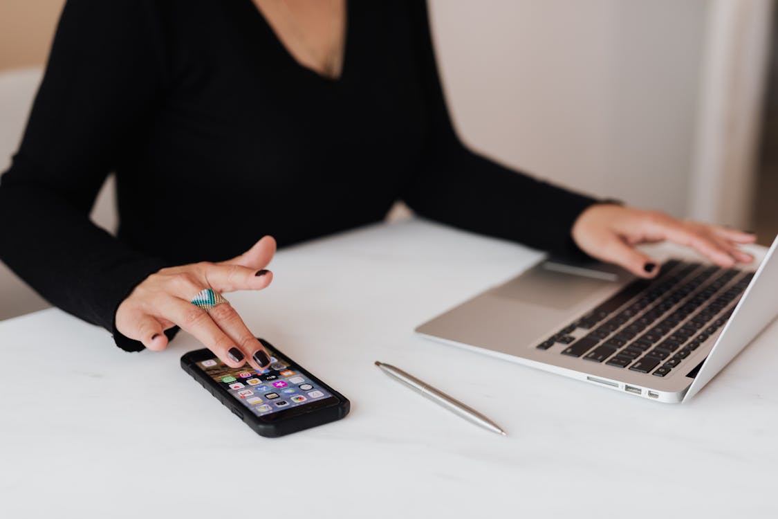 A professional is multitasking with a smartphone in one hand and working on a laptop with the other, indicative of the digital tools used by SEO specialists in the workplace.