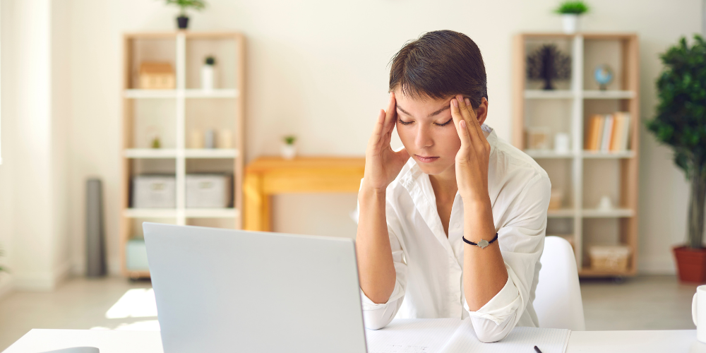 A distressed professional with hands on temples looking at a laptop screen, a portrayal of stress which may indicate challenges faced during employment or the process of termination.